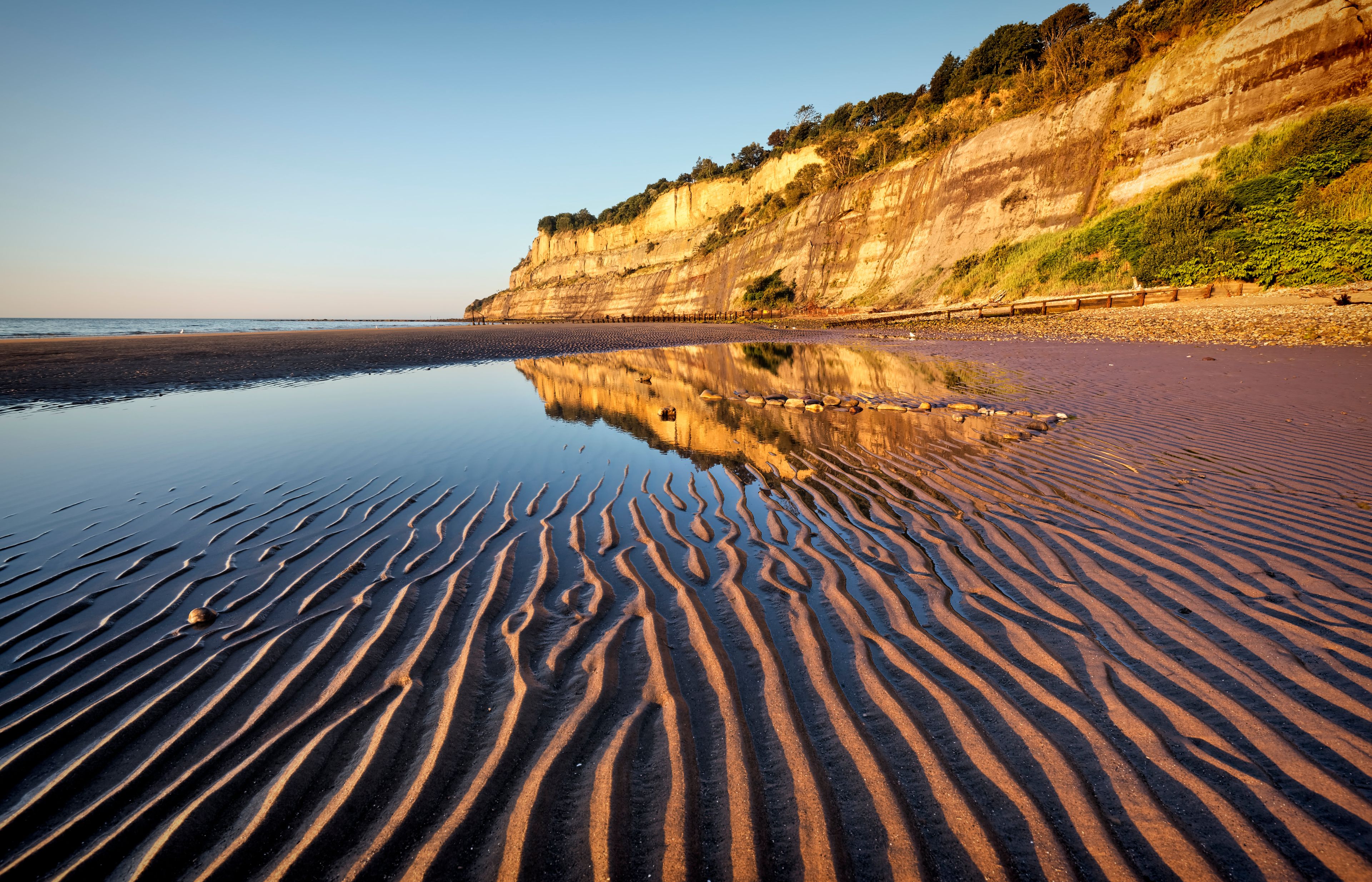 A beach with rippled sand patterns and a cliff in the background.