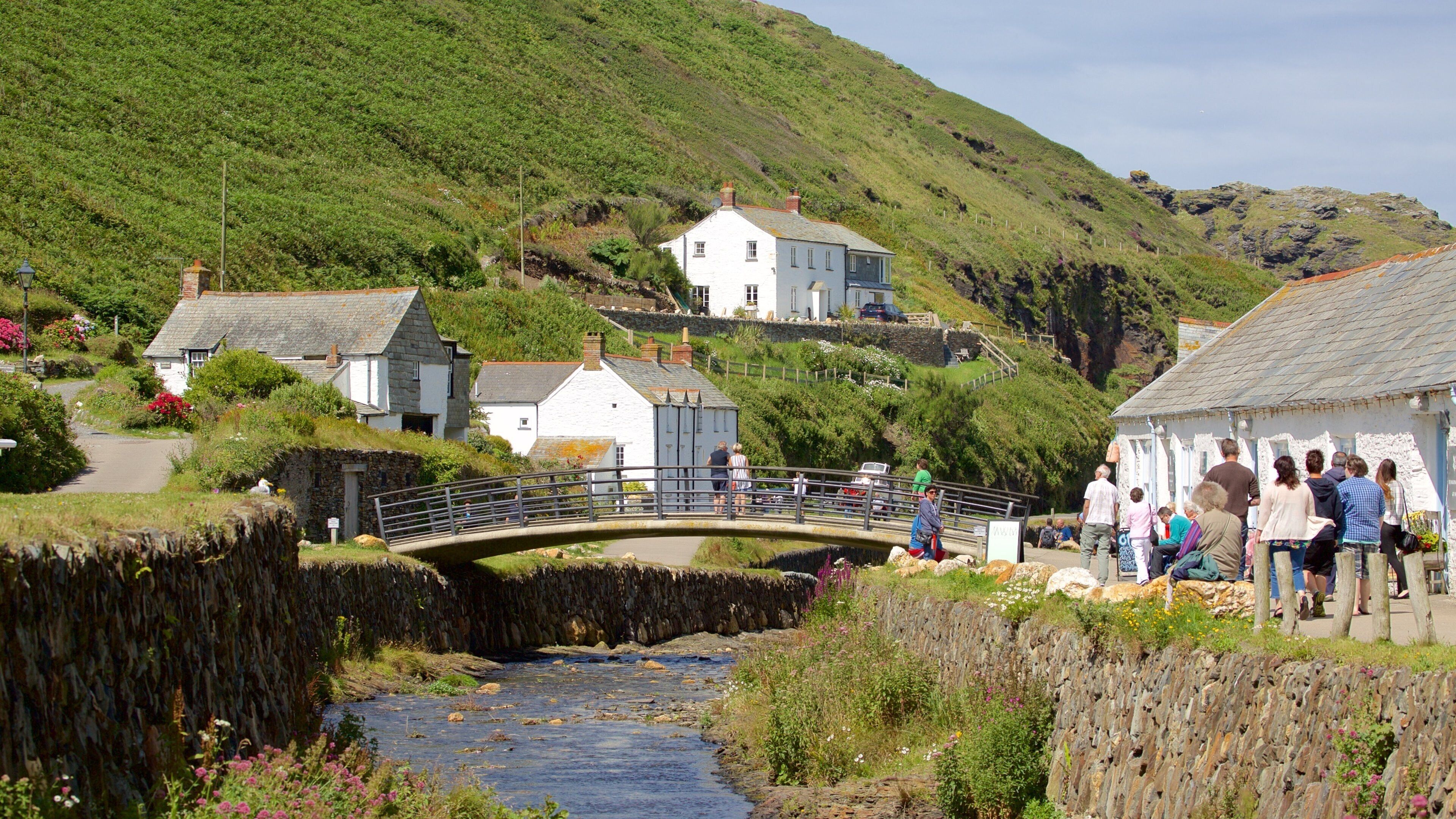 A stone bridge over a river, surrounded by lush greenery and houses on a hillside.