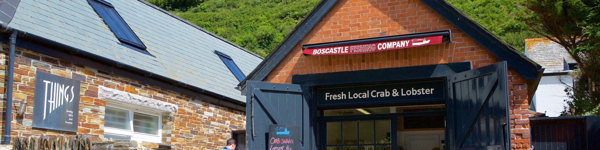 A coastal building with a sign for 'Boscattle Fishing Company' and 'Fresh Local Crab & Lobster'.