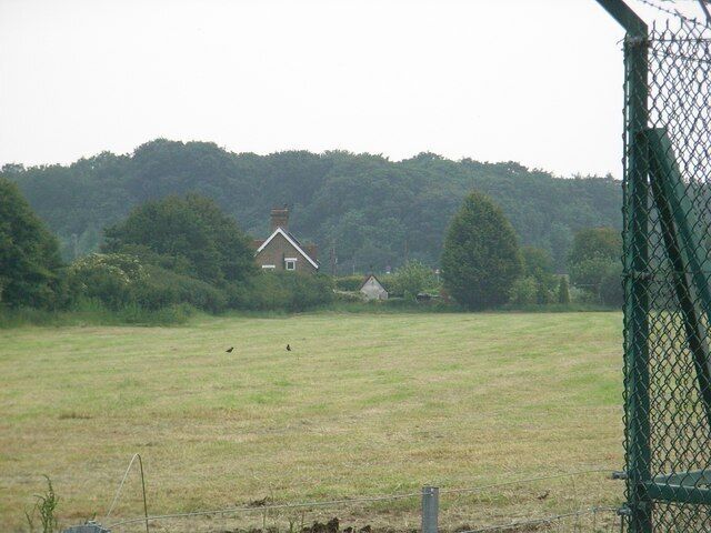 A rural landscape with a house, a fenced field, and a forest in the background.