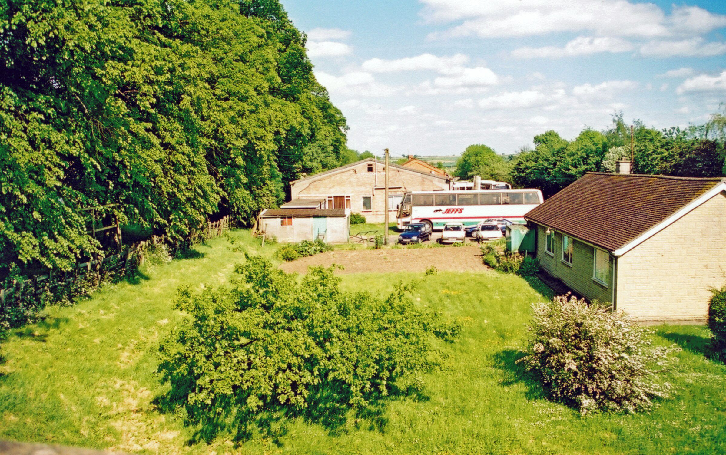 A rural landscape with a large tree, a bus, and a house.