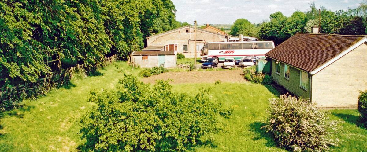 A rural landscape with a large tree, a bus, and a house.