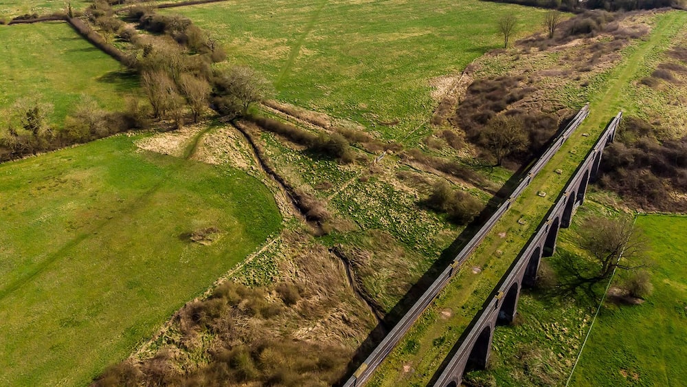Un viaduc surplombe un paysage rural, avec des champs et un petit village en arrière-plan.