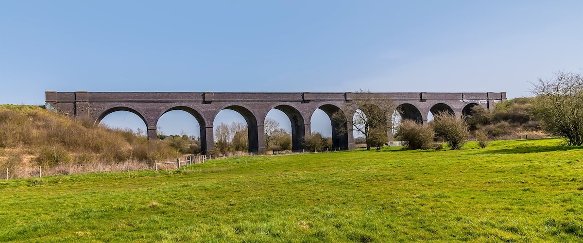 A large brick viaduct with multiple arches spanning a grassy field.