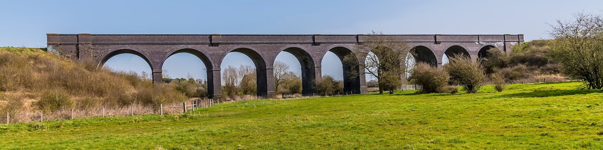 A large brick viaduct with multiple arches spanning a grassy field.