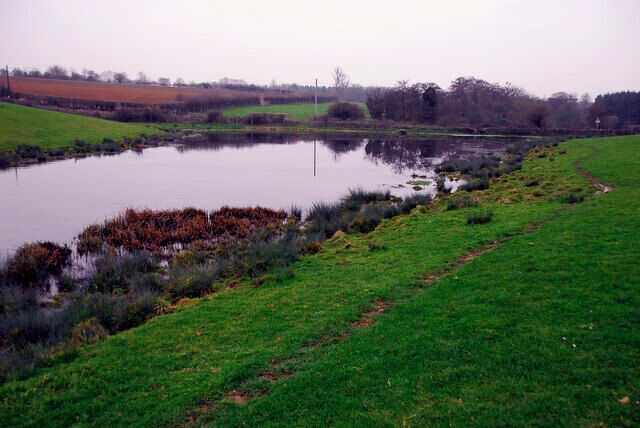 A pond surrounded by green fields and a dirt path.