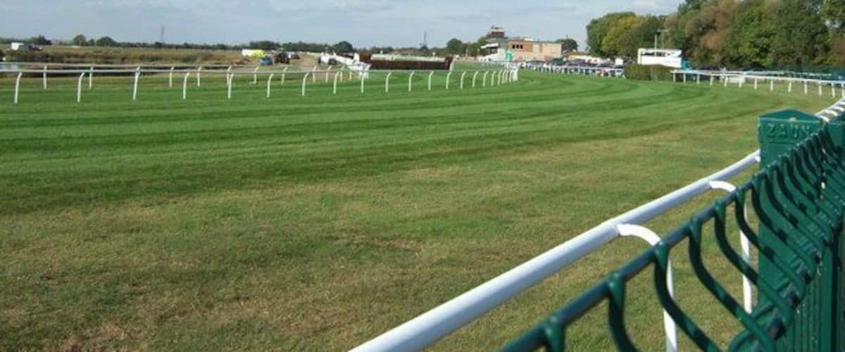 A grassy field with white fencing and a green barrier.