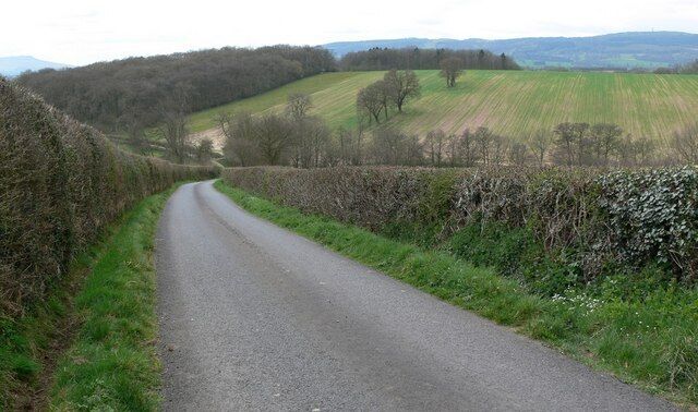 A narrow rural road flanked by stone walls and fields.