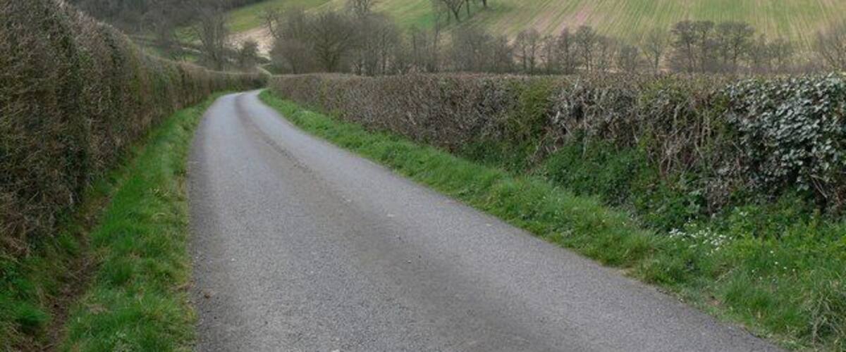 A narrow rural road flanked by stone walls and fields.