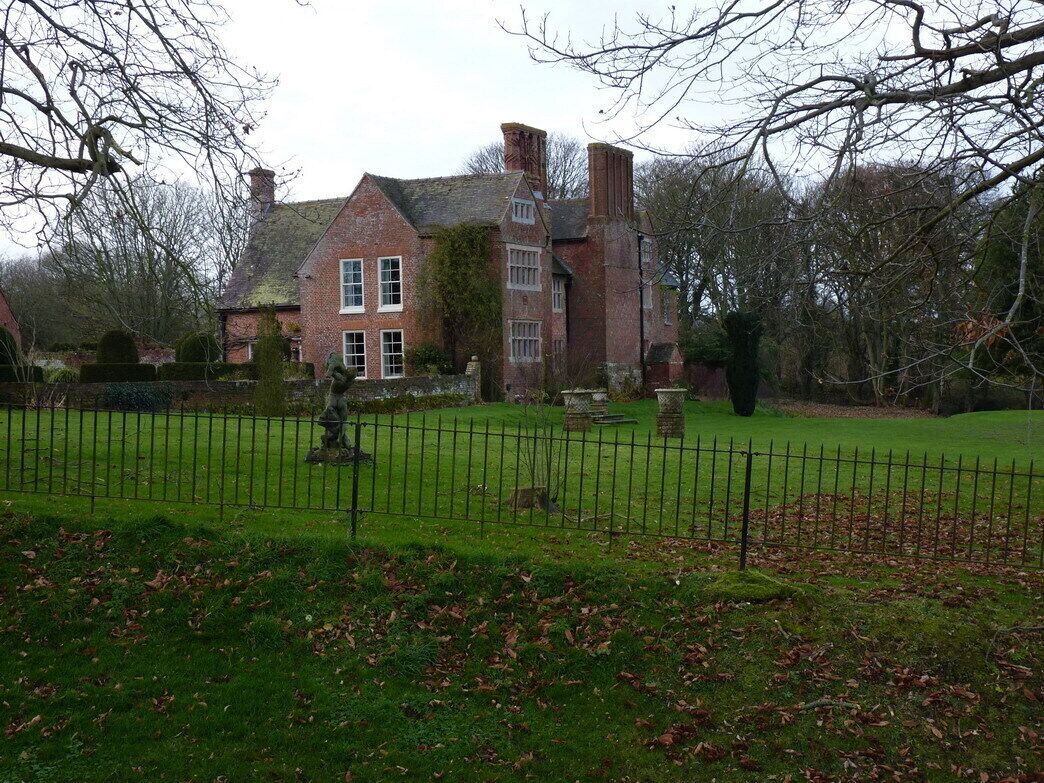 A large brick house with a well-maintained lawn and a stone statue in the foreground.