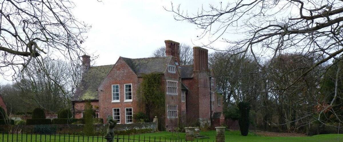A large brick house with a well-maintained lawn and a stone statue in the foreground.