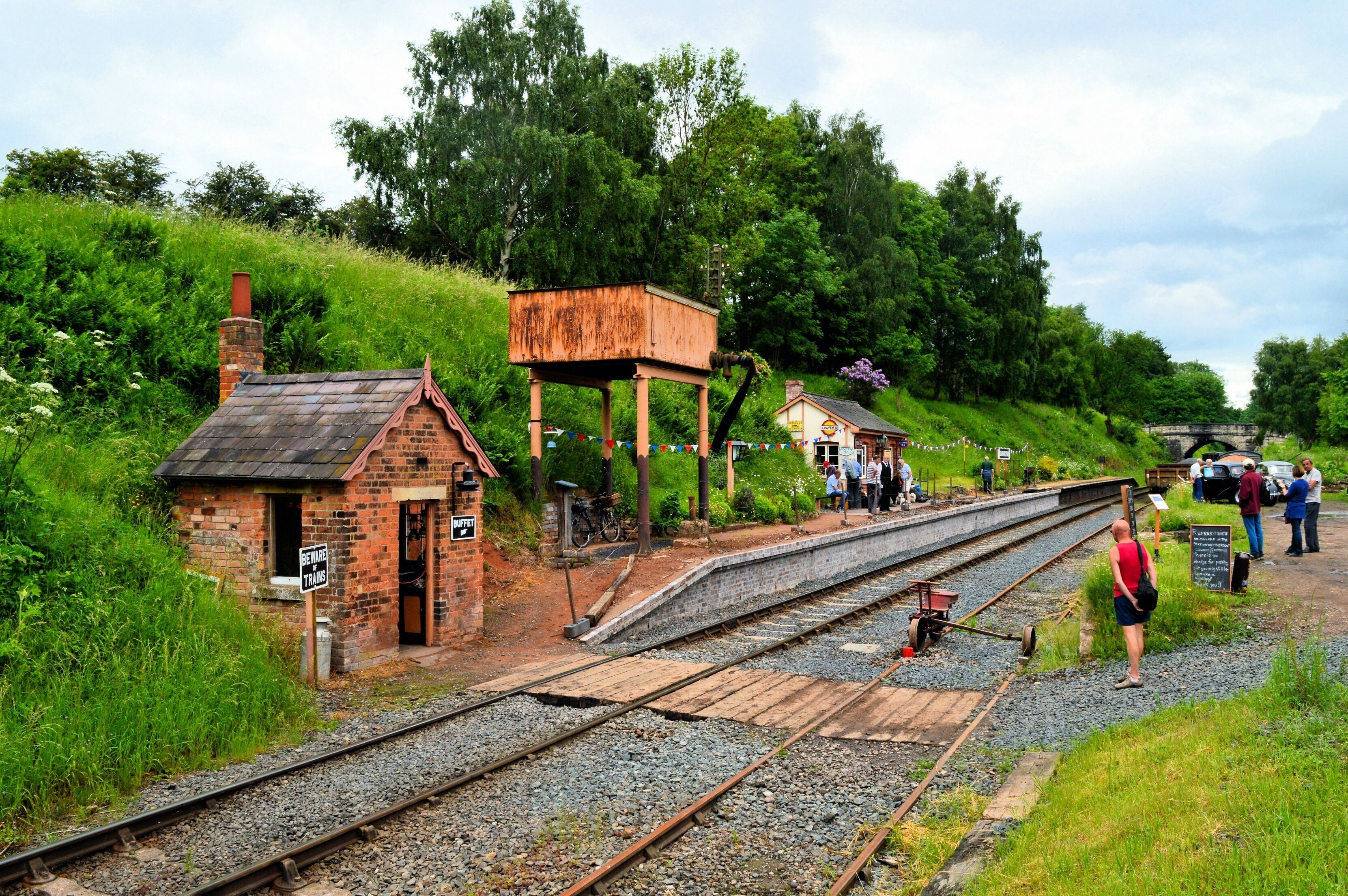 A small brick building with a sign reading "Beginner's Track" near railway tracks, surrounded by greenery and a stone bridge in the background.