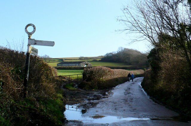 A rural road with a directional signpost, a puddle, and a distant building.