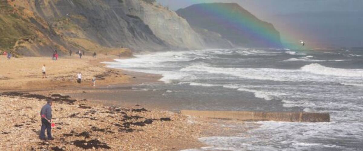 Rainbow at Charmouth Beach The rainbow appears to pass in front of the distant Golden Cap, the highest point on England's south coast. The rainbow is due to spray being whipped off the sea by high onshore winds.