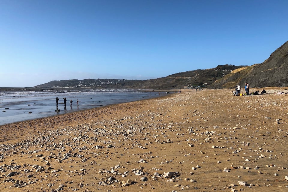 Une plage rocheuse parsemée de pierres, sous un ciel bleu dégagé.