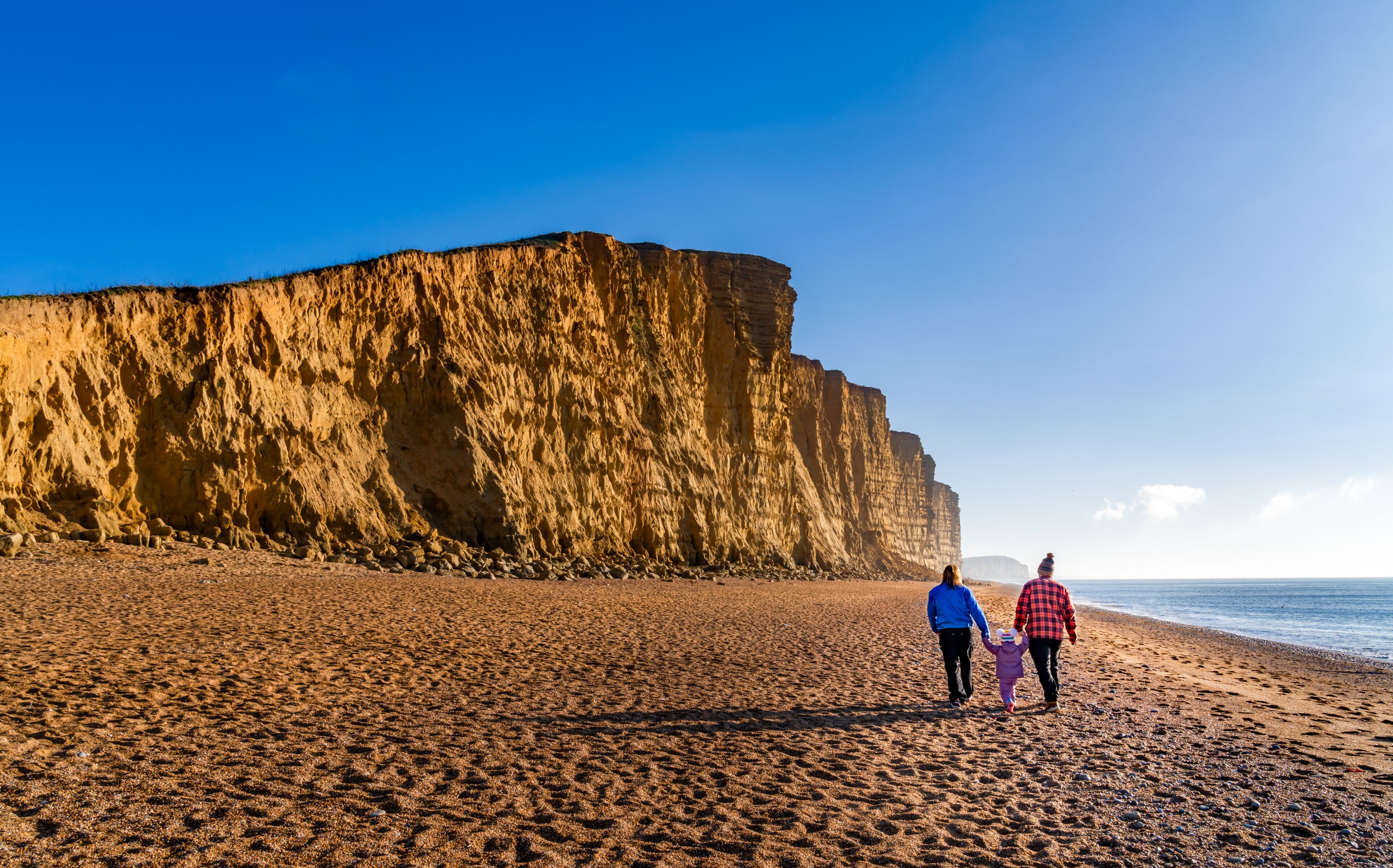 A sandy beach with a large cliff in the background.