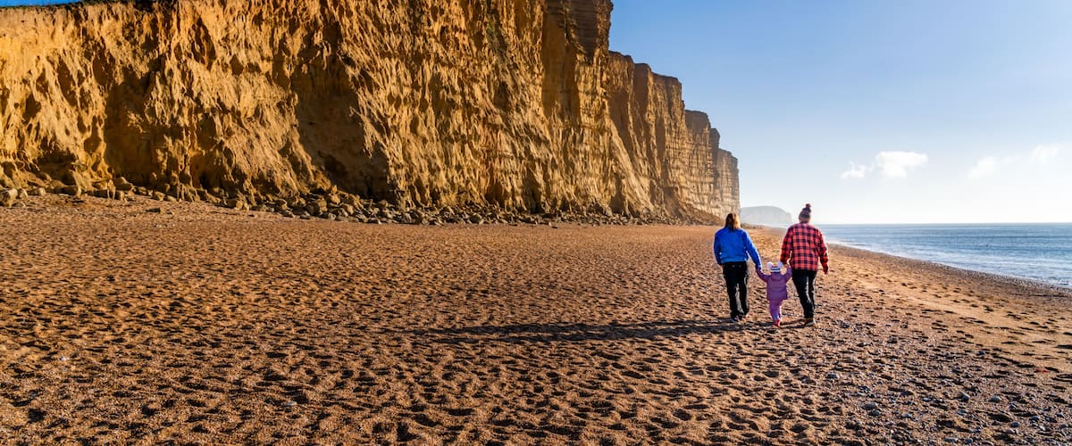 A sandy beach with a large cliff in the background.