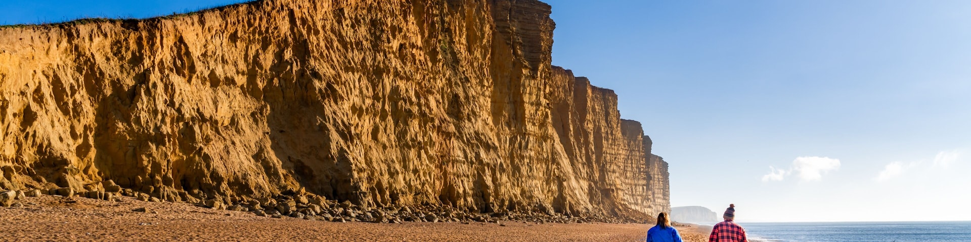 A sandy beach with a large cliff in the background.