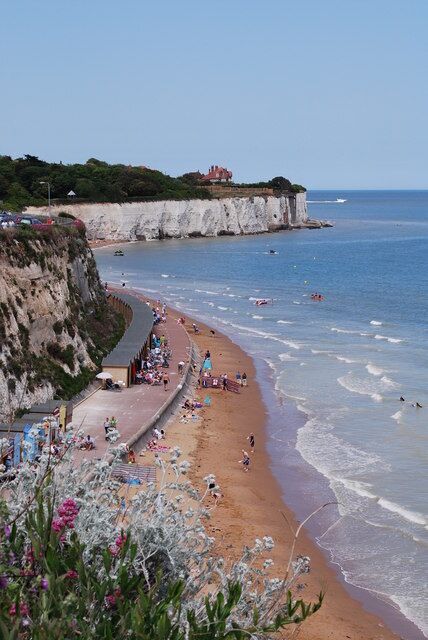 A coastal beach with cliffs, a sandy shore, and people enjoying the water.