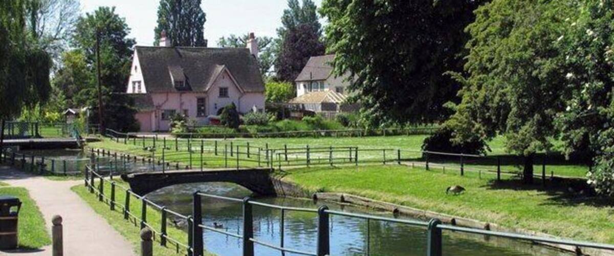 Un canal con un puente, un camino y casas al fondo.