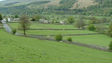 Un paysage rural caractérisé par des collines douces, des murets de pierre et une route sinueuse.