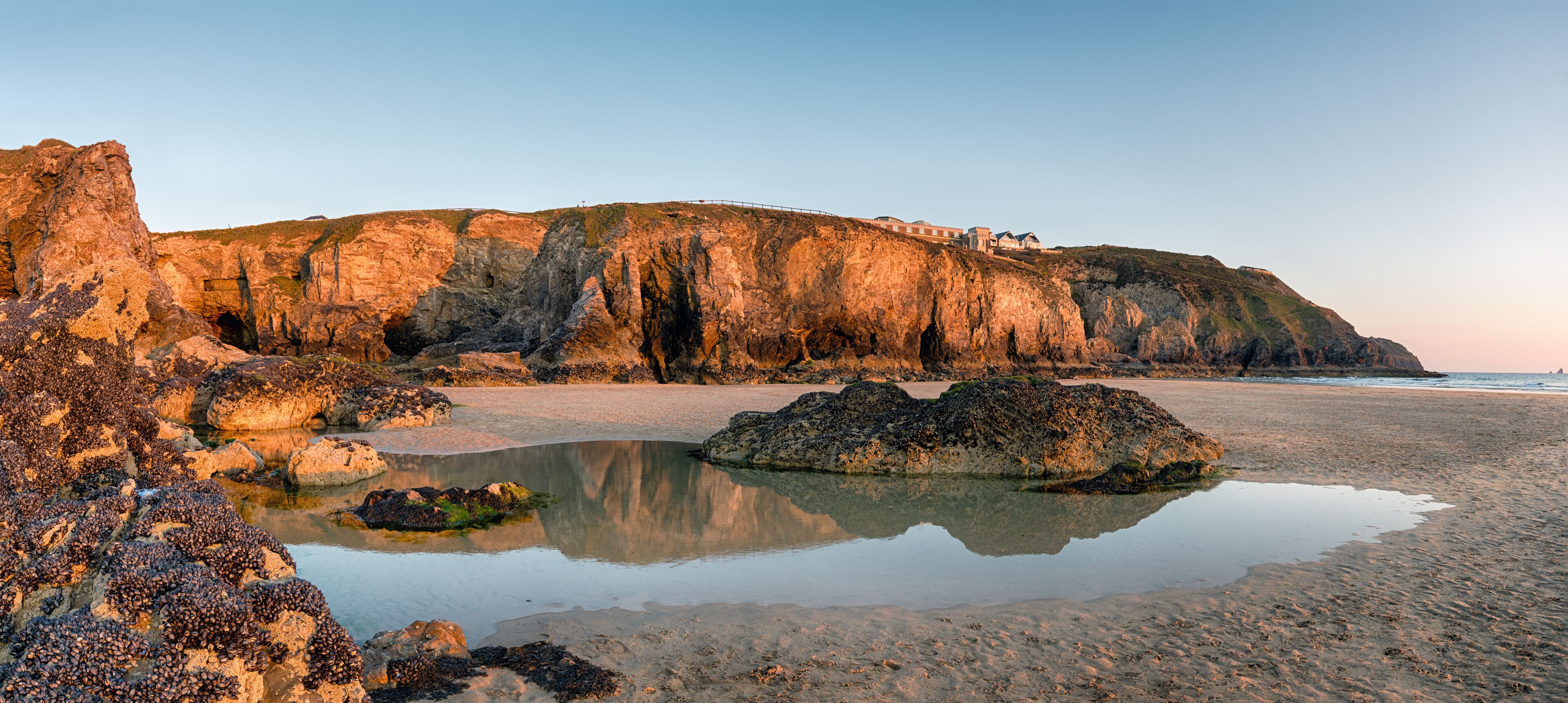 Un paisaje costero con acantilados rocosos, una playa y una masa de agua que refleja el entorno.