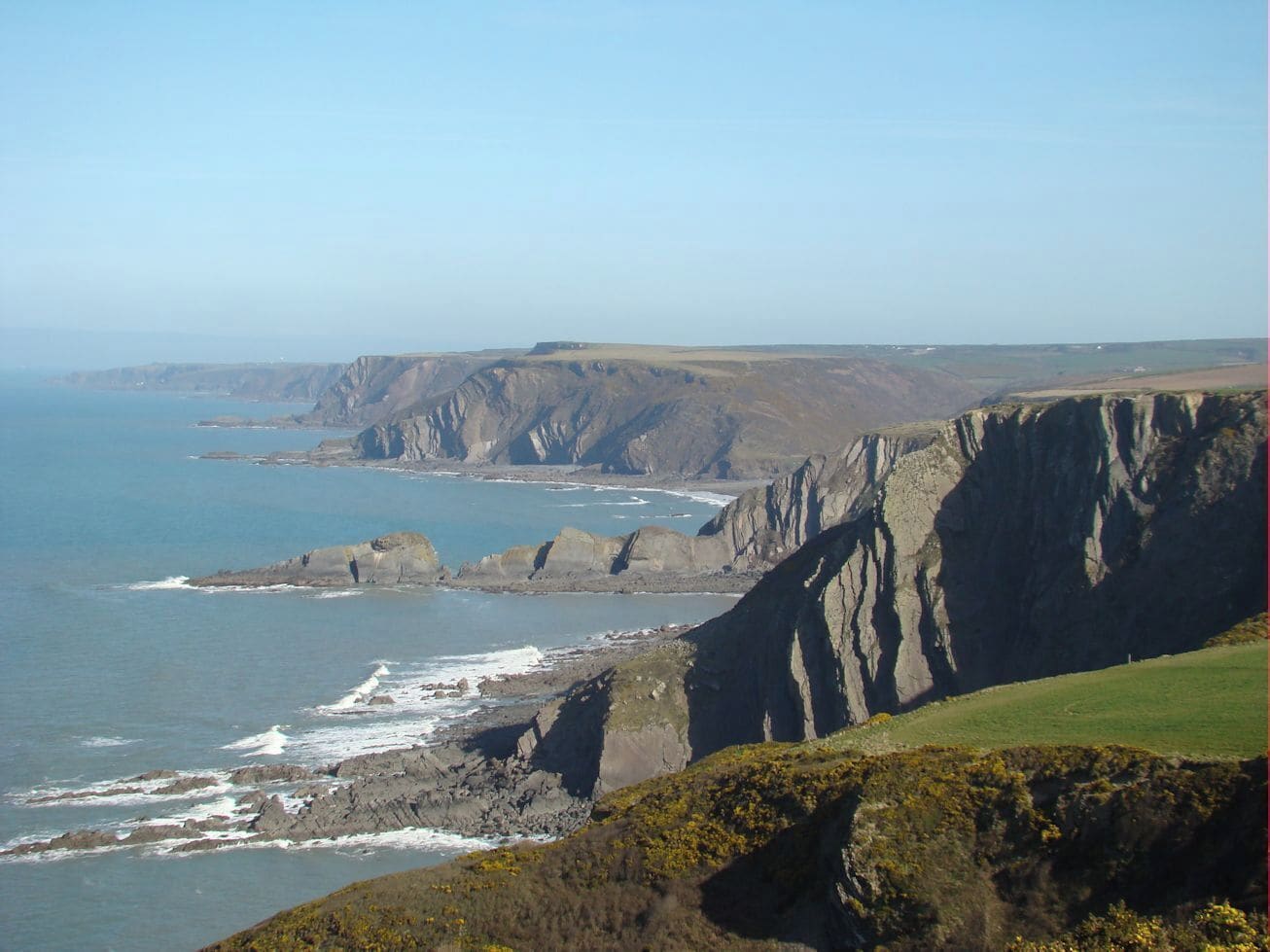A coastal cliff landscape with steep cliffs, a rocky shoreline, and a clear blue sky.