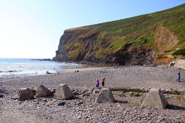 A pebbled beach with large rocks, a cliff, and the ocean.