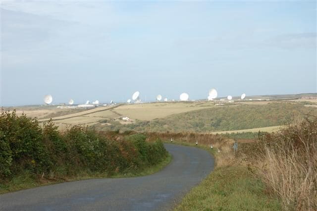 A rural landscape with a winding road, rolling hills, and multiple large white spherical structures in the distance.