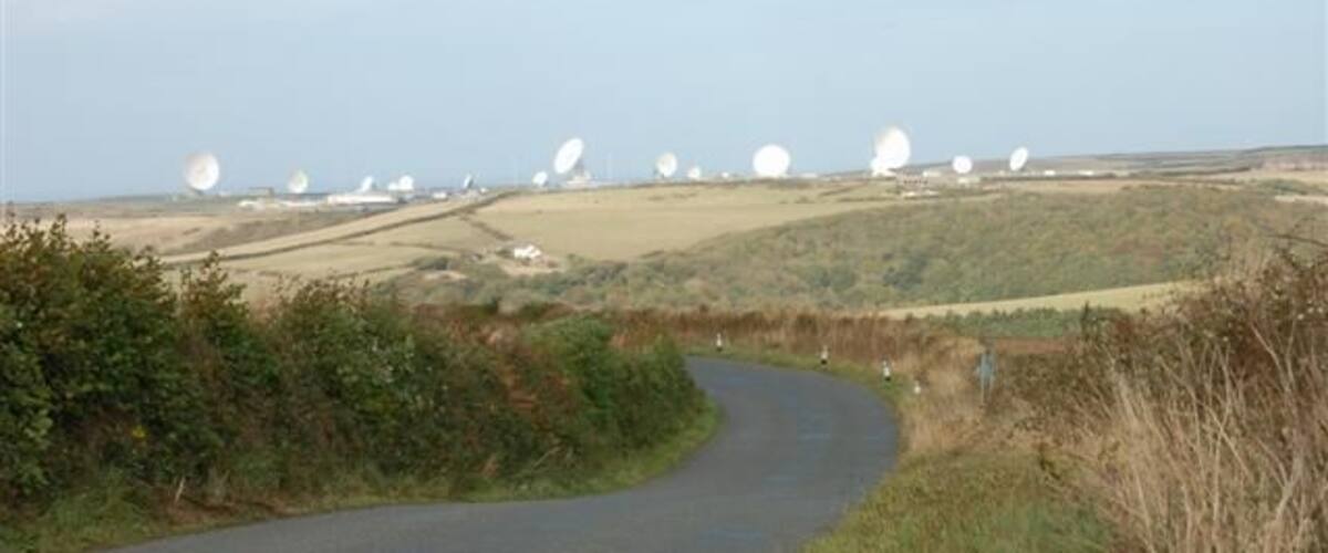 A rural landscape with a winding road, rolling hills, and multiple large white spherical structures in the distance.