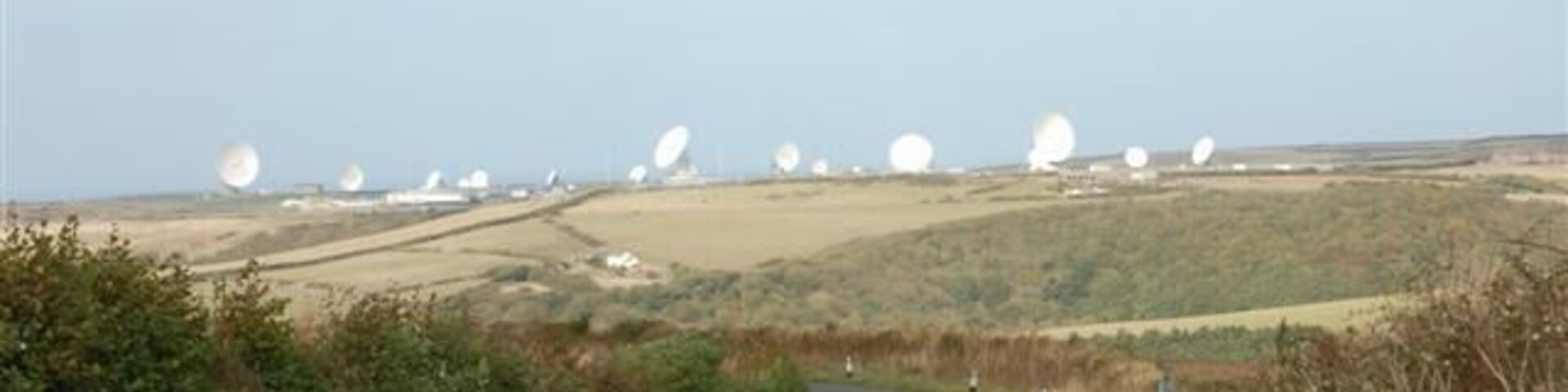 A rural landscape with a winding road, rolling hills, and multiple large white spherical structures in the distance.