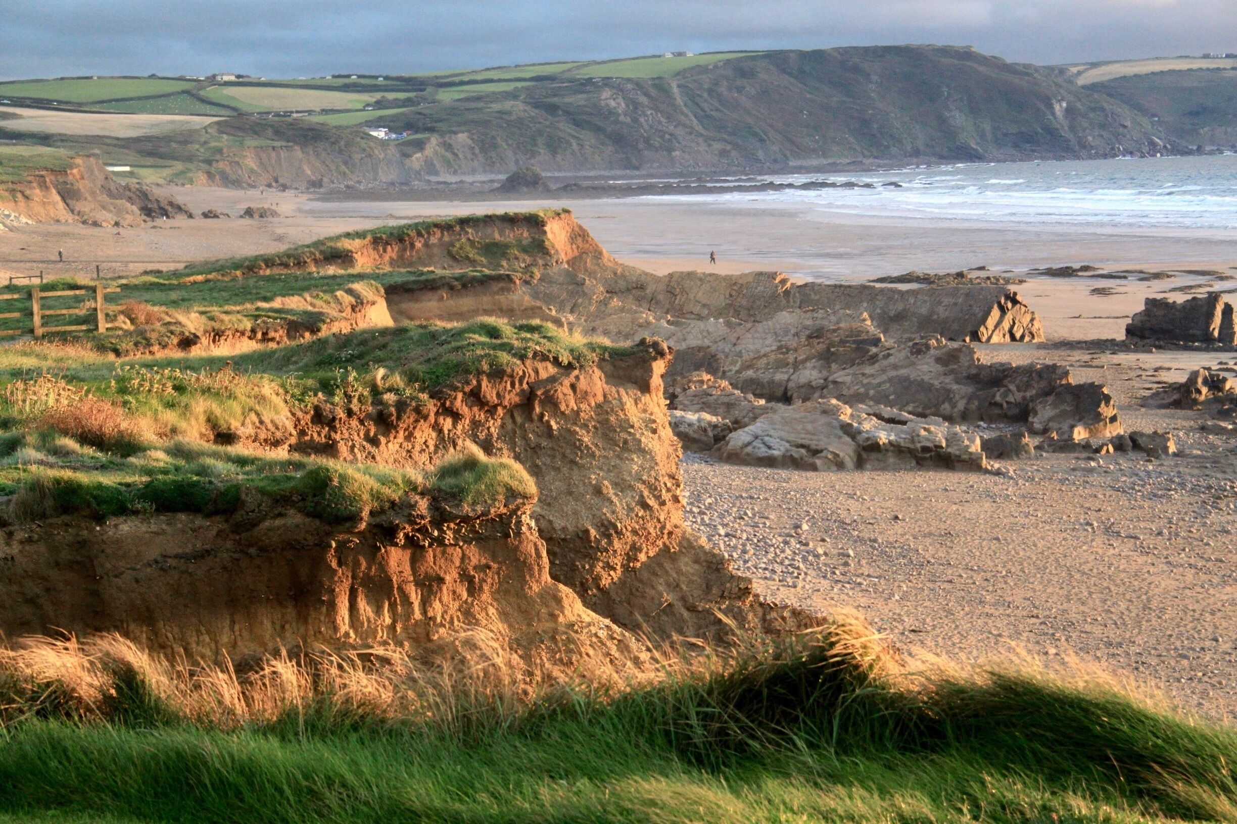 A coastal landscape with cliffs, a beach, and distant hills.