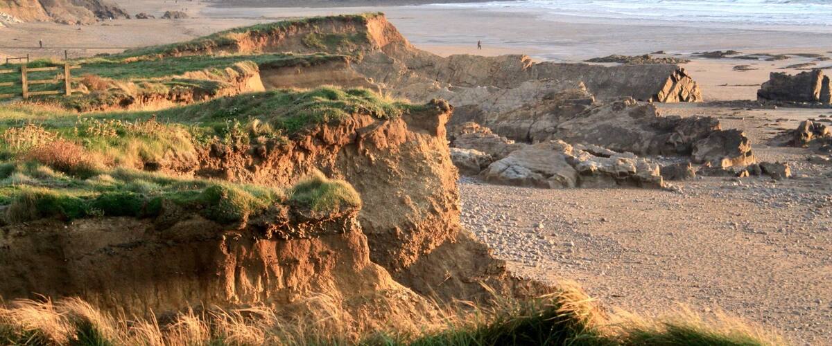 A coastal landscape with cliffs, a beach, and distant hills.