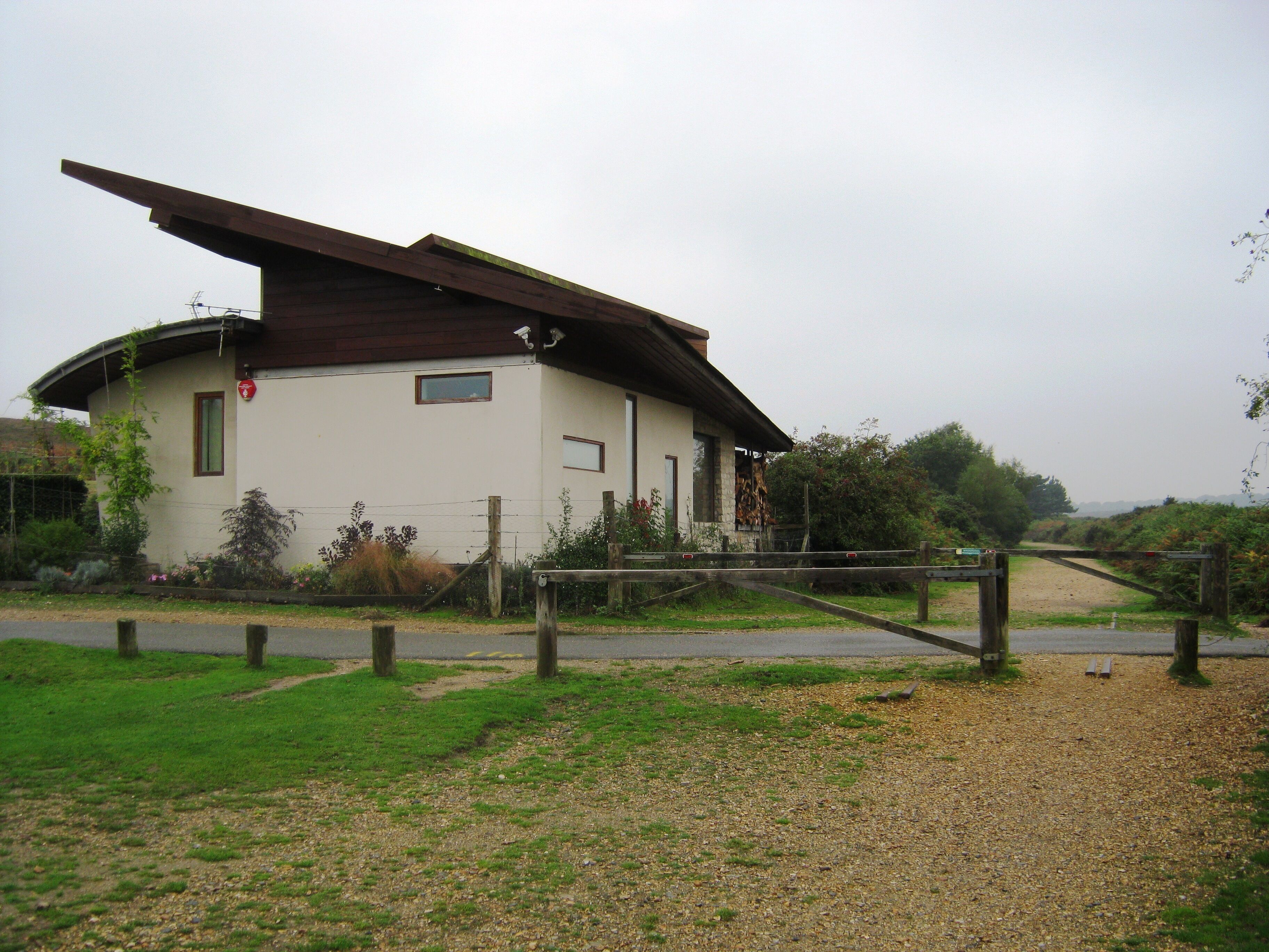 A small building with a sloped roof, surrounded by greenery and a gravel path.