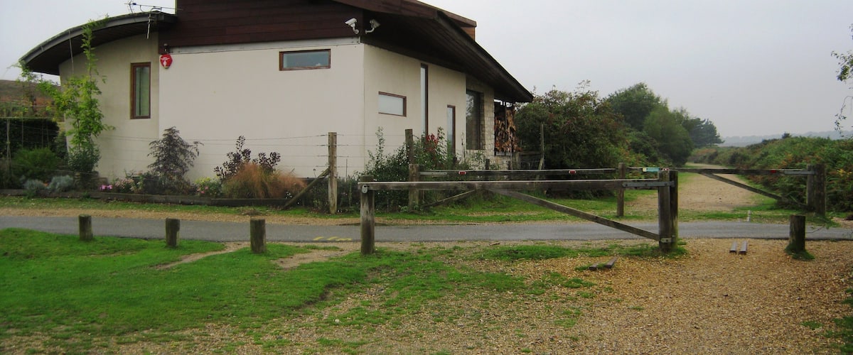 A small building with a sloped roof, surrounded by greenery and a gravel path.