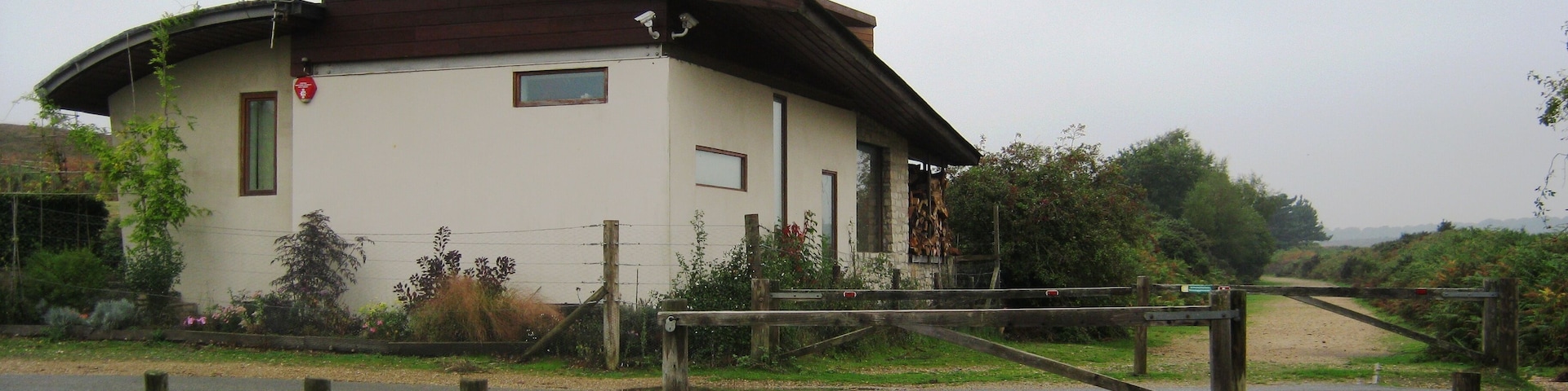 A small building with a sloped roof, surrounded by greenery and a gravel path.