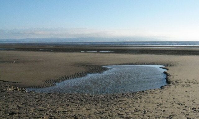 Berrow Flats Early evening with a rising tide. The setting sun provides dramatic lighting across the windswept sands while on the horizon is Exmoor and Hinkley Point Nuclear Power Station.