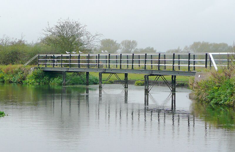 Trent and Mersey Canal near Wychnor, Staffordshire. The pound between Wychnor Lock and Alrewas Lock includes a short stretch about three hundred metres south-west of here where the canal merges with the River Trent, Consequently, here the actual water level fluctuates considerably after persistent heavy rain. The towpath (and public footpath) on the north side is built on stilts. At several points this effectively provides bridges across intermittent streams and other places where flood water flows off the plain, back to the river. These have now been given numbers, as if they were crossing the canal. The one in this picture is number 45C.
