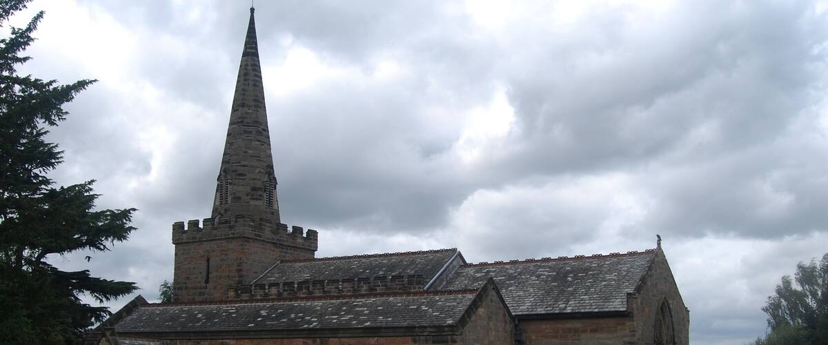 A historic church with a tall spire and a graveyard in front.