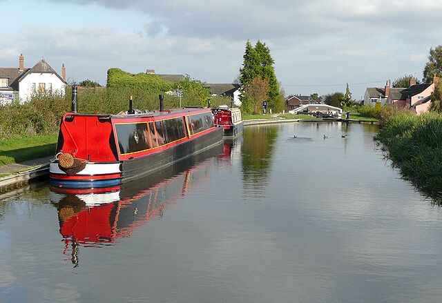 A narrow canal with a red and black boat docked on the left.