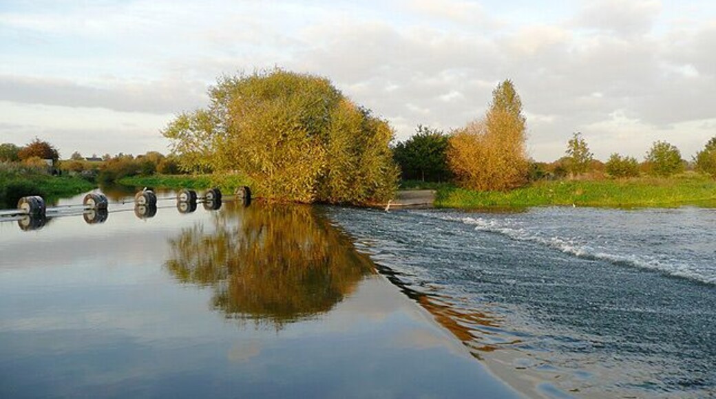 Canal, Boom, Weir and River. The weir was constructed to maintain a constant water level for the Trent and Mersey Canal, which uses the course of the River Trent for a short distance north of Alrewas. The boom on the left prevents canal boats from being swept onto the weir. To the left of the boom, the river level is maintained by the canal as far as Wychnor Lock. This picture was taken with the sun low, in late evening, hence the golden glow to the trees. A lone heron stands, maybe hoping for a final catch in the fading rays of sunlight.