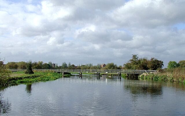 The River Trent near Alrewas, Staffordshire. This is the scene approaching Alrewas from the north-east. The river flows towards the camera, through the low walkway/bridge which is the towpath for the Trent and Mersey Canal. The canal veers off to the left towards Alrewas Lock, having utilised the river's course for about three hundred metres. This pound of the canal is not navigable safely when the river is in flood.