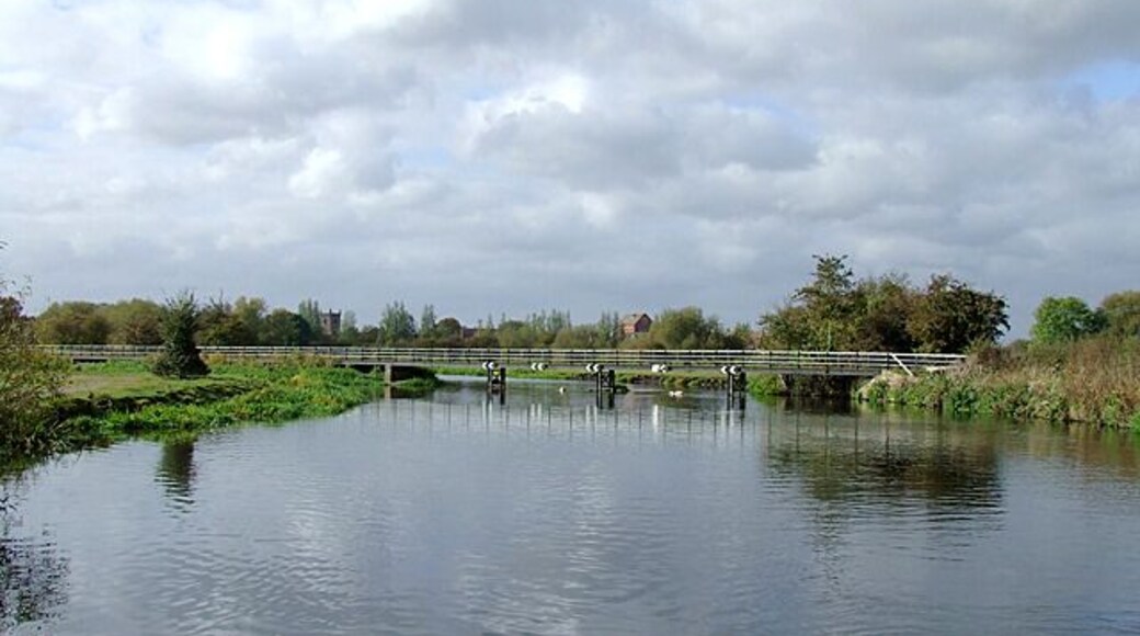 The River Trent near Alrewas, Staffordshire. This is the scene approaching Alrewas from the north-east. The river flows towards the camera, through the low walkway/bridge which is the towpath for the Trent and Mersey Canal. The canal veers off to the left towards Alrewas Lock, having utilised the river's course for about three hundred metres. This pound of the canal is not navigable safely when the river is in flood.