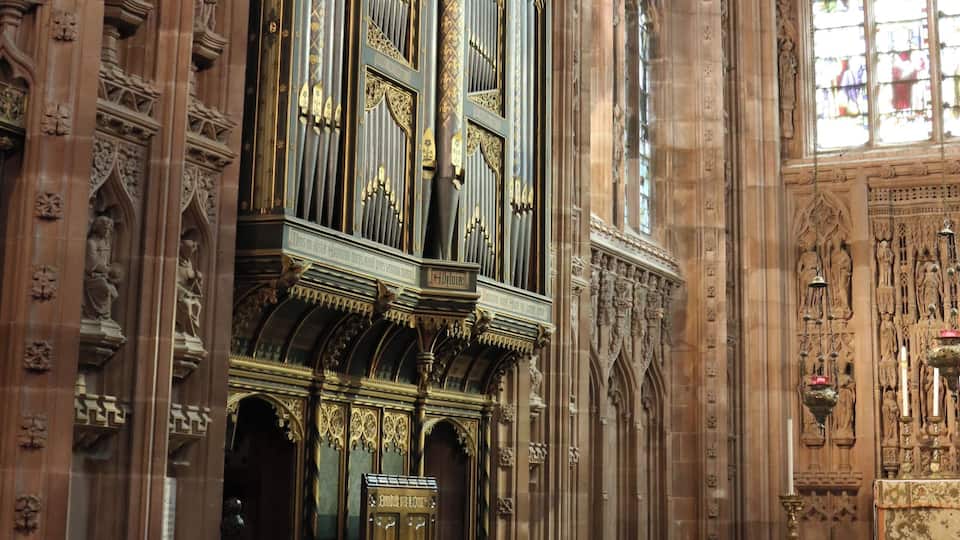 An ornate church interior with a large organ, arched windows, and intricate stone carvings.