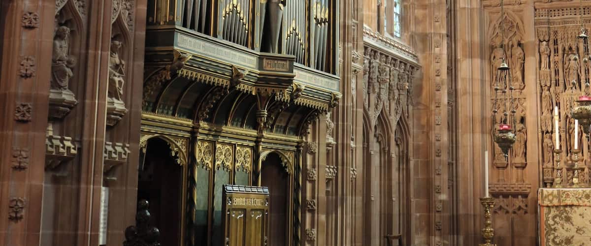 An ornate church interior with a large organ, arched windows, and intricate stone carvings.