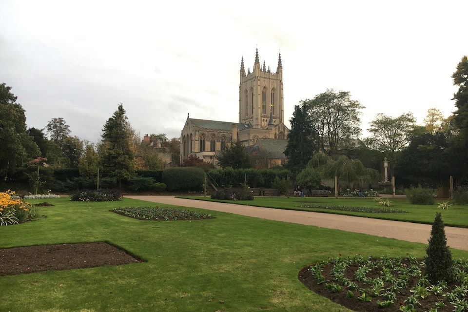 A well-maintained garden with a pathway leading to a historic church with a tall spire.