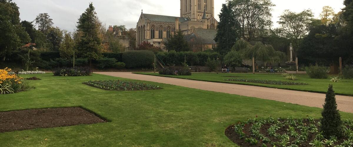 A well-maintained garden with a pathway leading to a historic church with a tall spire.