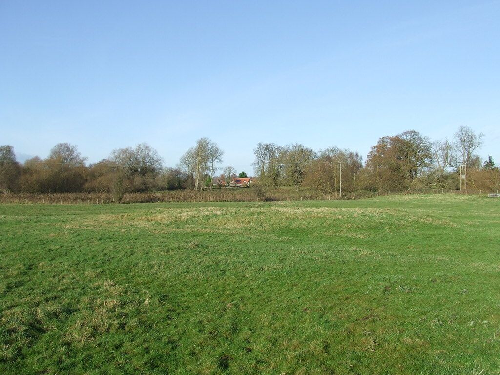 A green field with a red house in the distance and trees around.