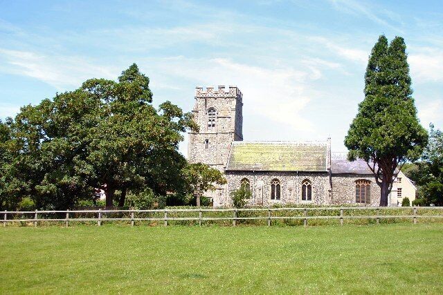 A stone church with a bell tower and a large tree in the foreground.