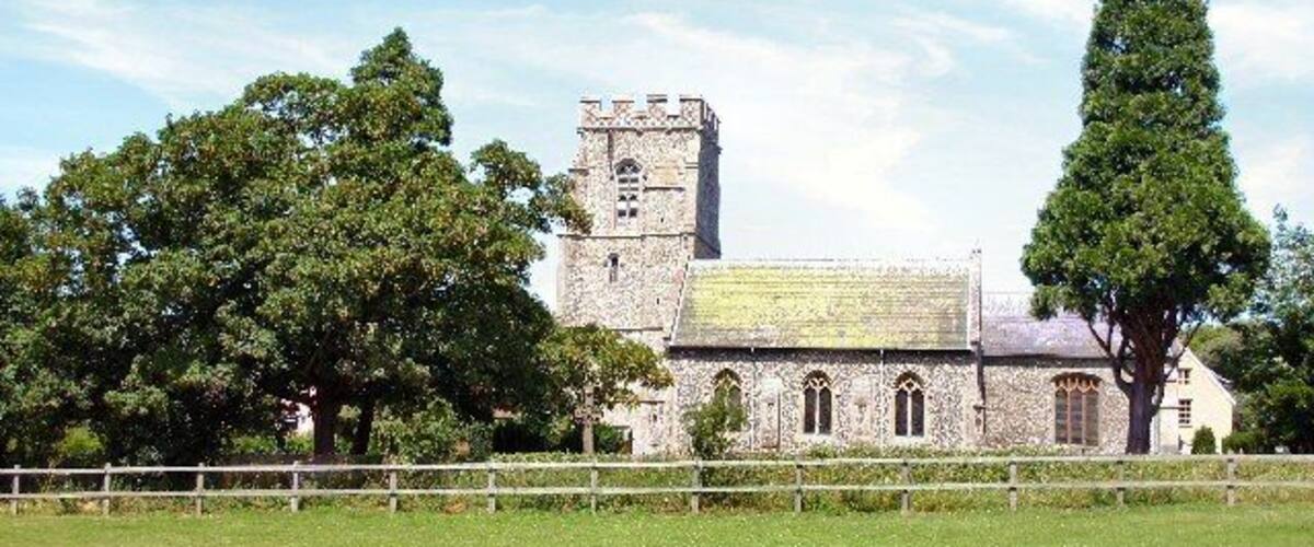 A stone church with a bell tower and a large tree in the foreground.
